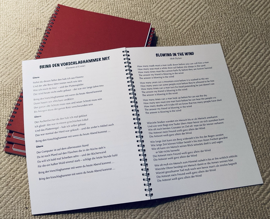 broschüren in wird-o-bindung mit liedtexten für die teilnehmenden bei meinen mitsing-abenden … ein kleiner stapel auf hellem teppich … das oberste exemplar ist aufgeschlagen … man sieht die songs „bring den vorschlaghammer mit“ und „blowing in the wind“