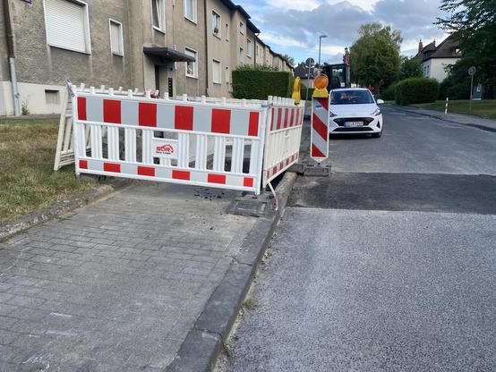 Eine Baustellenabsicherung an einem Gehweg. Die Baustelle ist nur mangelhaft abgesichert. Es fehlt eine Rampe, die es ermöglicht am Bordstein herunterzukommen.