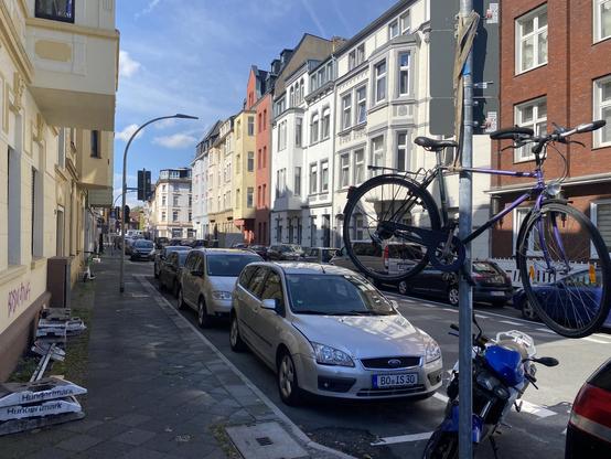 Straßenszene mit zahlreichen geparkten Autos . Ein Fahrrad ist auf einem Verkehrsschild in die Höhe gehangen worden.
