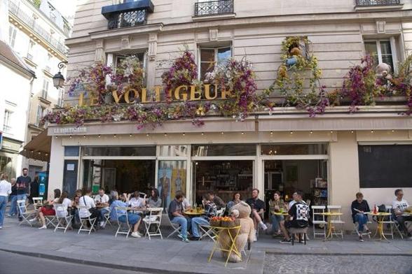 Foto eines Cafés. die Tische sind fast alle besetzt. An einem Tisch wurde ein Stoffbär gesetzt. Auf dem Tisch vor ihm stehen Pakete mit Gemüse zum Mitnehmen.