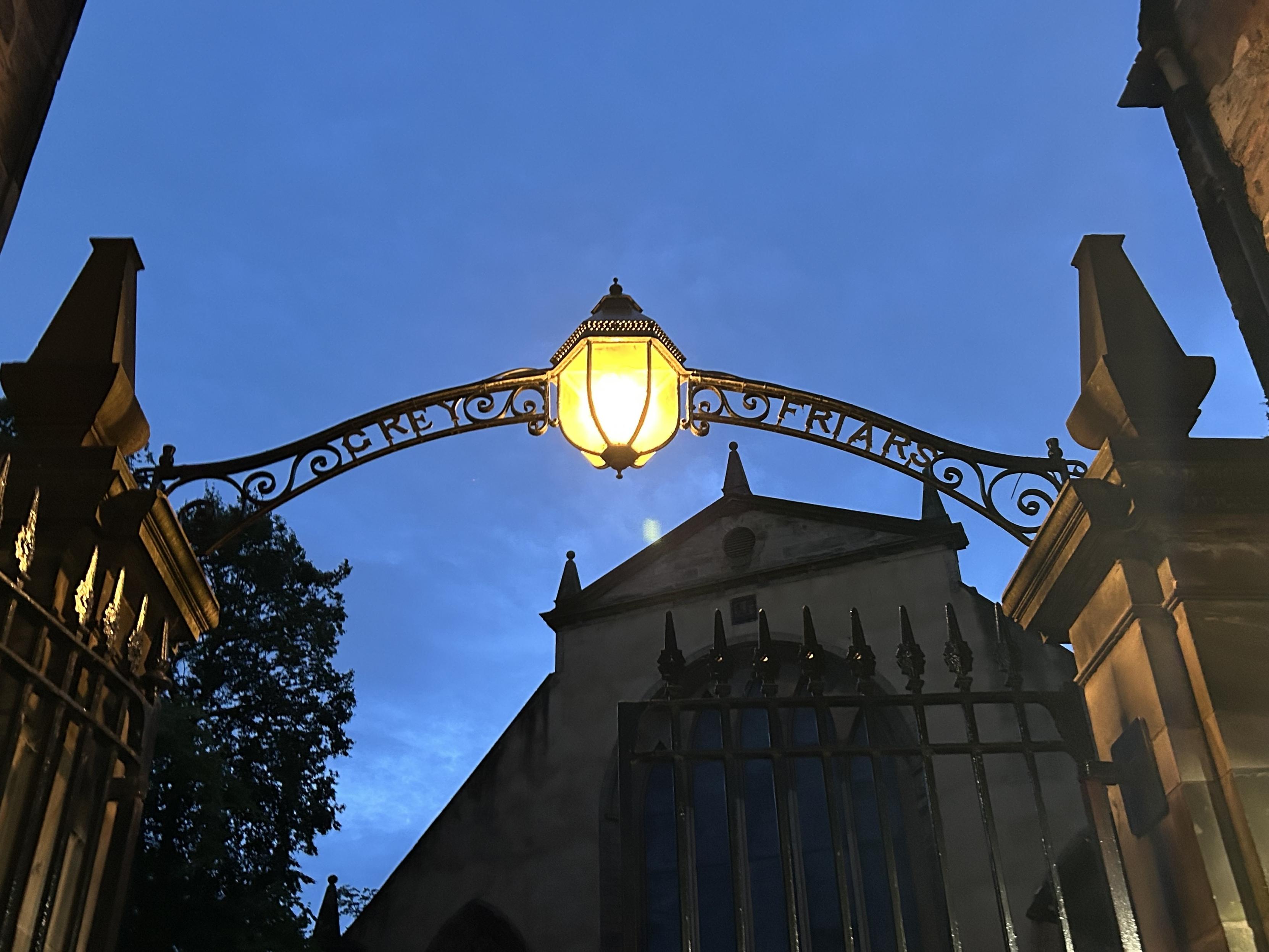 An ornate wrought-iron archway with a lantern is illuminated against a twilight sky. The archway features the word "Friars," and a historical building is visible in the background, partially obscured by trees.
Ein kunstvoller schmiedeeiserner Torbogen mit einer Laterne wird vor einem Dämmerungshimmel beleuchtet. Der Torbogen trägt das Wort "Bröde", und im Hintergrund ist ein historisches Gebäude sichtbar, das teilweise von Bäumen verdeckt wird. An ornate wrought-iron archway with a lantern is illuminated against a twilight sky. The archway features the word "Friars," and a historical building is visible in the background, partially obscured by trees.
Ein kunstvoller schmiedeeiserner Torbogen mit einer Laterne wird vor einem Dämmerungshimmel beleuchtet. Der Torbogen trägt das Wort "Bröde", und im Hintergrund ist ein historisches Gebäude sichtbar, das teilweise von Bäumen verdeckt wird.
