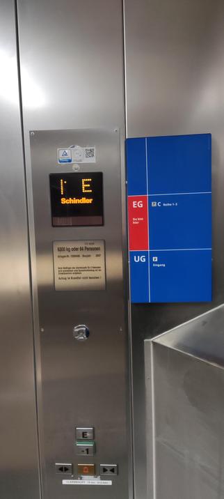 Foto des Innenraums eines Aufzugs bei IKEA. Neben den Wahltastern für die Etagen ist ein  Hinweisschild zu den einzelnen Etagen angebracht, bei dem das Erdgeschoss farblich und mit dem Text "Sie befinden sich hier" hervorgehoben ist.