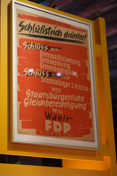 Ein gerahmtes Poster mit auffälliger roter und schwarzer Schrift. Der Hintergrund ist orangefarben, und das Poster spiegelt historische politische Themen wider.

Text:

Schlussstrich drünter!
Schluss mit-
Entnazifizierung
Entrechtung
Entmündigung
Schluss mi dem
Staatsbürger 2-Klasse
WER
Staatsbürgerliche Gleichberechtigung
WILL
Wählt
FDP
BISHER LDP