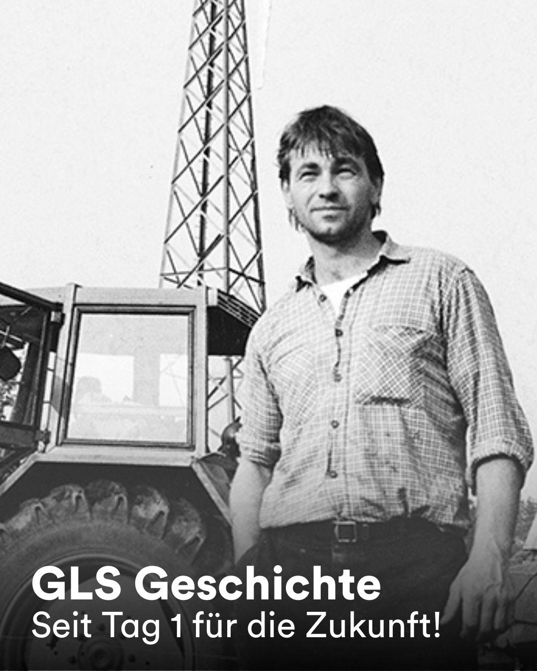 Ein schwarz-weiß Foto zeigt eine Person vor einem Traktor. Im Hintergrund ist ein Windrad. Text: 'GLS Geschichte Seit Tag 1 für die Zukunft!'