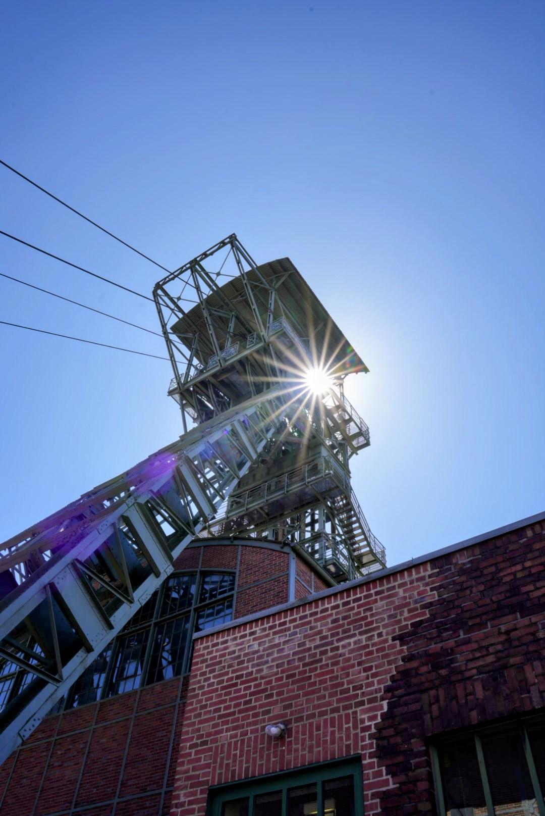 Förderturm der Zeche Zollern von unten fotografiert. Die Sonne steht direkt hinter dem Turm und ist als Sonnenstern sichtbar.