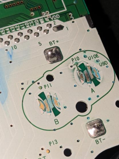Foto einer Platine eines GameBoy Colors. Zu sehen sind die Leiterbahnen unter den A und B Knöpfen. Die Felder, die von den Tasten verbunden werden, sind abgerieben. Eine weiße Lackschicht (?) deckt fast alle anderen Flächen der Platine ab.
