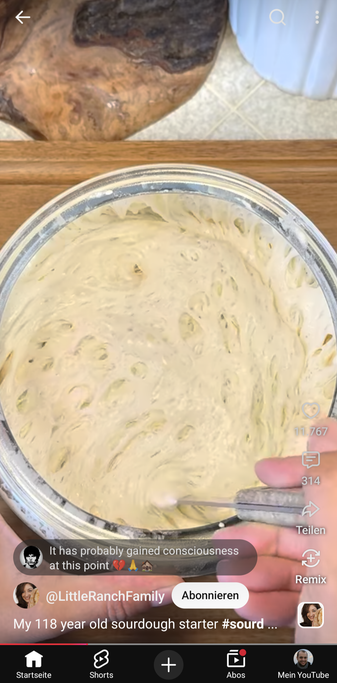 Screenshot aus dem verlinkten Video, man sieht einen Sauerteigstarter von oben in einem Glas, eine Hand rührt mit einer Kelle den Teig um. Man sieht sehr viele Blasen mit großem Volumen im Teig, der förmlich zerfällt.