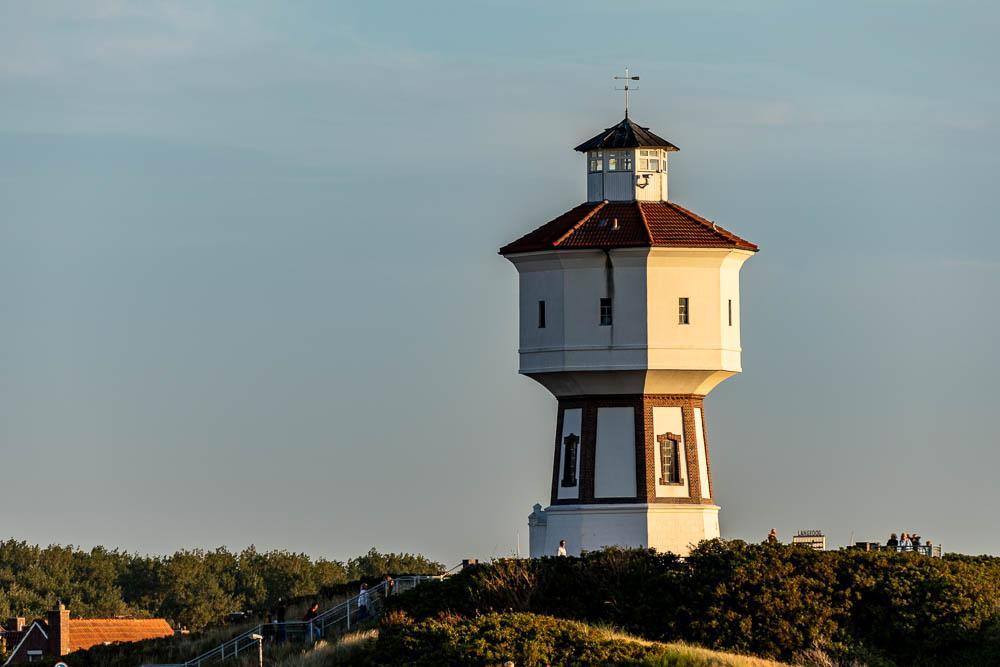 Der historische Wasserturm von Langeoog steht im warmen Abendlicht über den Dünen, im Hintergrund ein weiter Himmel.